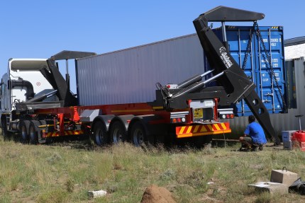 Vrachtwagen takelt een container op zijn laadvlak.
